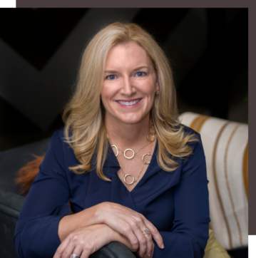 Smiling blonde woman in a navy blue blouse sitting indoors.